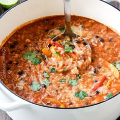 a spoon in a bowl filled with mexican chicken and rice soup, garnished with cilantro