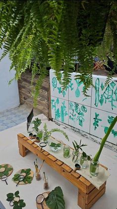 a table topped with lots of green plants and vases filled with plant life sitting on top of a wooden bench