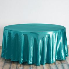 a round table covered with a teal satin tablecloth in front of a white wall