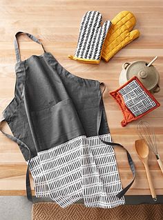 aprons and kitchen utensils laid out on a wooden table with an oven mitt