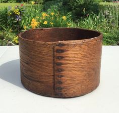 a wooden basket sitting on top of a white table next to some flowers and bushes