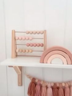 a white shelf topped with wooden toys and pink tassels on top of it