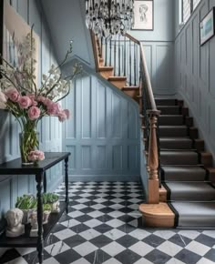 a staircase with chandelier and flowers in vases on the table next to it