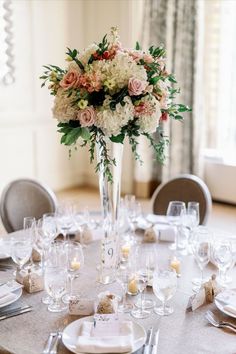 a table is set with white and pink flowers in a tall vase on top of it