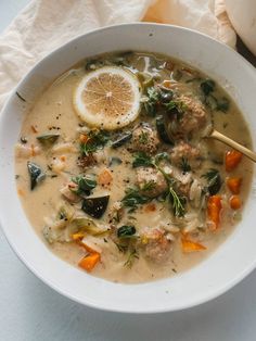 a white bowl filled with meat and vegetable soup next to a slice of lemon on top of a napkin