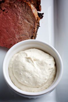 a white bowl filled with cream cheese next to sliced meat