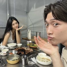 two people sitting at a table with food in front of them and one person holding his hand up to the camera