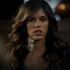 a beautiful young woman with long brown hair and blue eyes looking at the camera while standing in a dark room