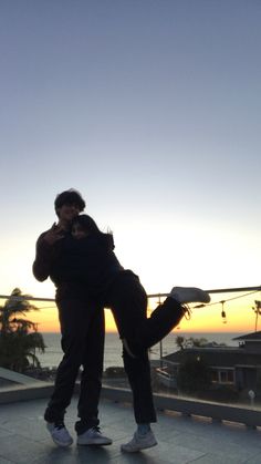 two people hugging each other while standing on top of a roof with the sun setting in the background