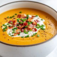 a white bowl filled with carrot soup topped with bacon and chives, garnished with chopped green onions