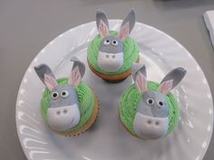 three decorated cupcakes on a white plate with green frosting and bunny ears