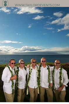 a group of men standing next to each other in front of the ocean with leis around their necks