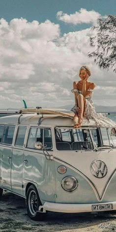 a woman sitting on top of an old vw camper van in front of the ocean