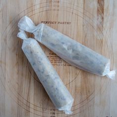 two packaged sausages sitting on top of a wooden cutting board