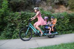 a woman riding a bike with two children in the back