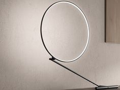 a modern desk lamp with a circular light on it's side, in front of a white wall