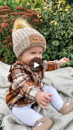 a baby sitting on top of a blanket wearing a hat and holding his hand out