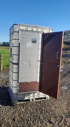 a white outhouse sitting on top of a dirt field next to a green field