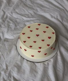 a white cake with red hearts on it sitting on top of a sheet covered table