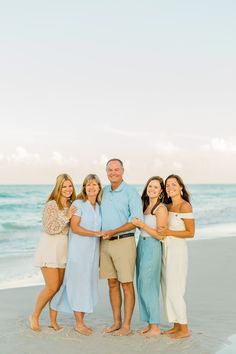 a group of people standing on top of a sandy beach next to the ocean with their arms around each other