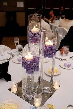 two tall clear vases filled with flowers and candles on top of a white table