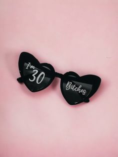 two black heart shaped sunglasses with the words i'm 30 written on them against a pink background