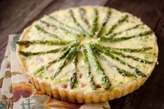 a quiche with asparagus and cheese on top sits on a tablecloth