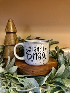 a white coffee mug with the words i smell snow on it sitting next to some green leaves