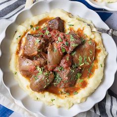 a white plate topped with mashed potatoes covered in meat and gravy on top of a blue and white table cloth