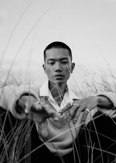 a young man sitting in tall grass holding his hands together