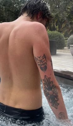 a man is in the water with his back turned to the camera and tattoos on his arm