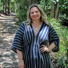 a woman standing on a path in the woods wearing a blue and white striped dress