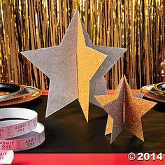 three silver and gold stars next to each other on a table with some measuring tape