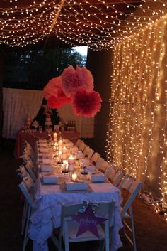 a long table is set with white linens and lite - up lights in the background