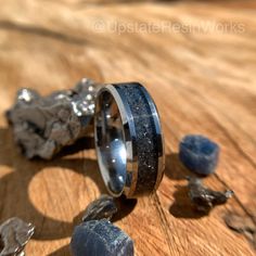 a wedding ring sitting on top of a wooden table next to some rocks and stones