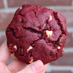 a hand holding a chocolate chip cookie in front of a brick wall with white chips on it