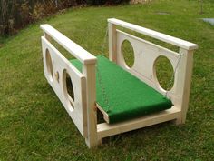 a wooden bench with a green cushion on the seat and chain attached to it, sitting in grass