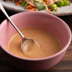 a pink bowl filled with soup next to a plate full of salad on a table