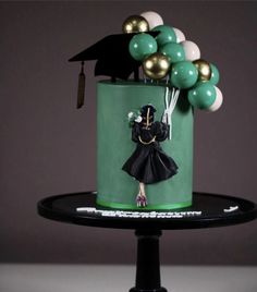 a graduation cake with balloons and a graduate's cap on top, sitting on a pedestal