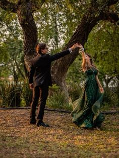 a man and woman in formal wear dancing under the tree's branches at sunset