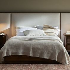 a bed with two nightstands and pillows on top of it in a room that has carpeted flooring