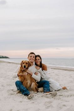 a man and woman sitting on the beach with their dog