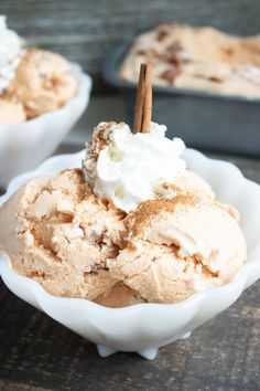 two bowls filled with ice cream on top of a wooden table and cinnamon sticks sticking out of them