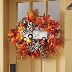 a front door decorated with an autumn wreath and monogrammed pumpkins, pine cones, and plaid ribbon