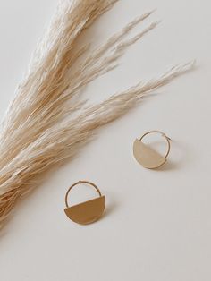 two small gold hoop earrings on top of a white table next to some dry grass