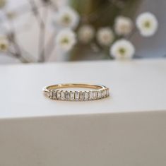 a gold ring with baguettes on top of it and flowers in the background