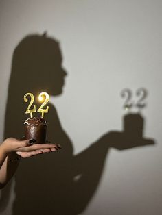 a person holding a cake with the number twenty two on it in front of a shadow