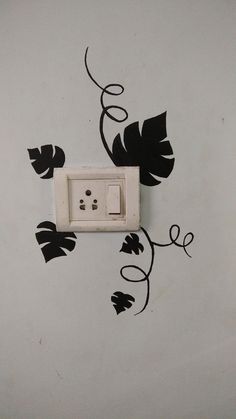 an electrical outlet is decorated with black leaves and vines on a white wall in the corner of a room