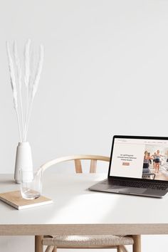 an open laptop computer sitting on top of a wooden table next to a vase with white flowers