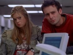 two people looking at a computer screen in an office building, one person is frowning and the other looks concerned